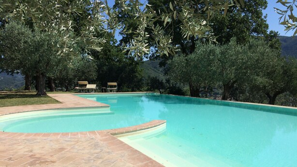 A clear swimming pool with a tiled deck, surrounded by trees and a view of a mountainous landscape. - Old Country House and pool In Umbrian Hills Between Foligno And Assisi (Foligno)