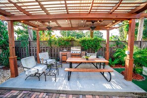 A covered patio with a wooden table and chairs, a grill, and a pergola with string lights. - Inn The Heights - Apt 2 (Tampa)