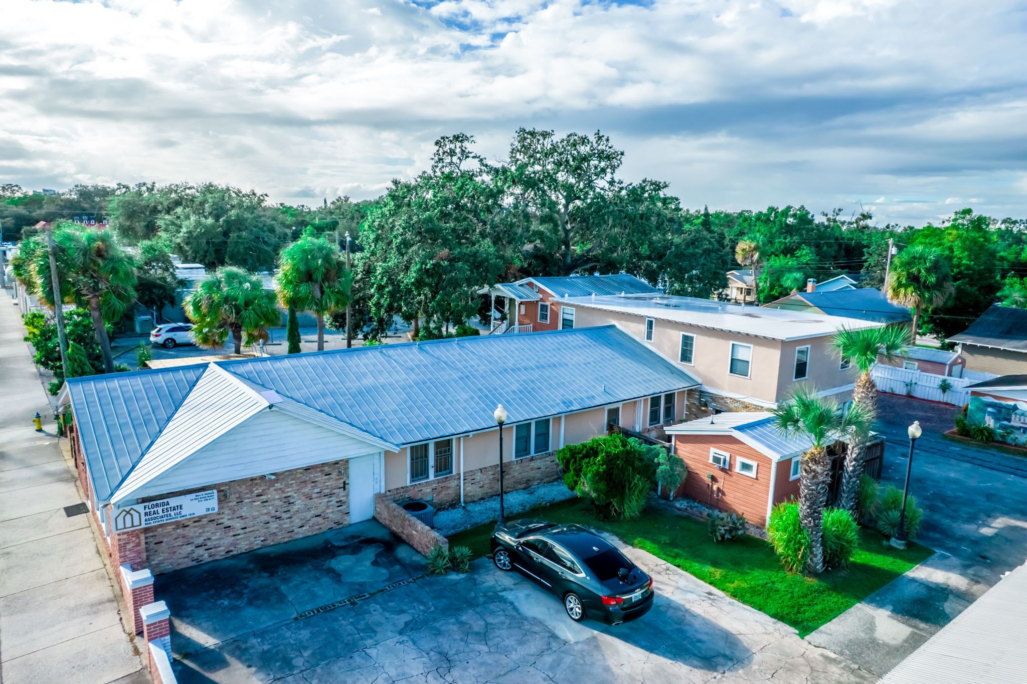 A two-story brick building with a metal roof, a parked car, and a well-maintained lawn.