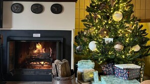 Ein gemütliches Wohnzimmer mit Kamin, einem geschmückten Weihnachtsbaum und einem Kaminbrett mit verschiedenen Dekorationen.
