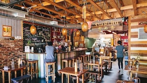 L’intérieur d’un restaurant avec des tables et des bancs en bois, un coin bar et des lanternes suspendues.