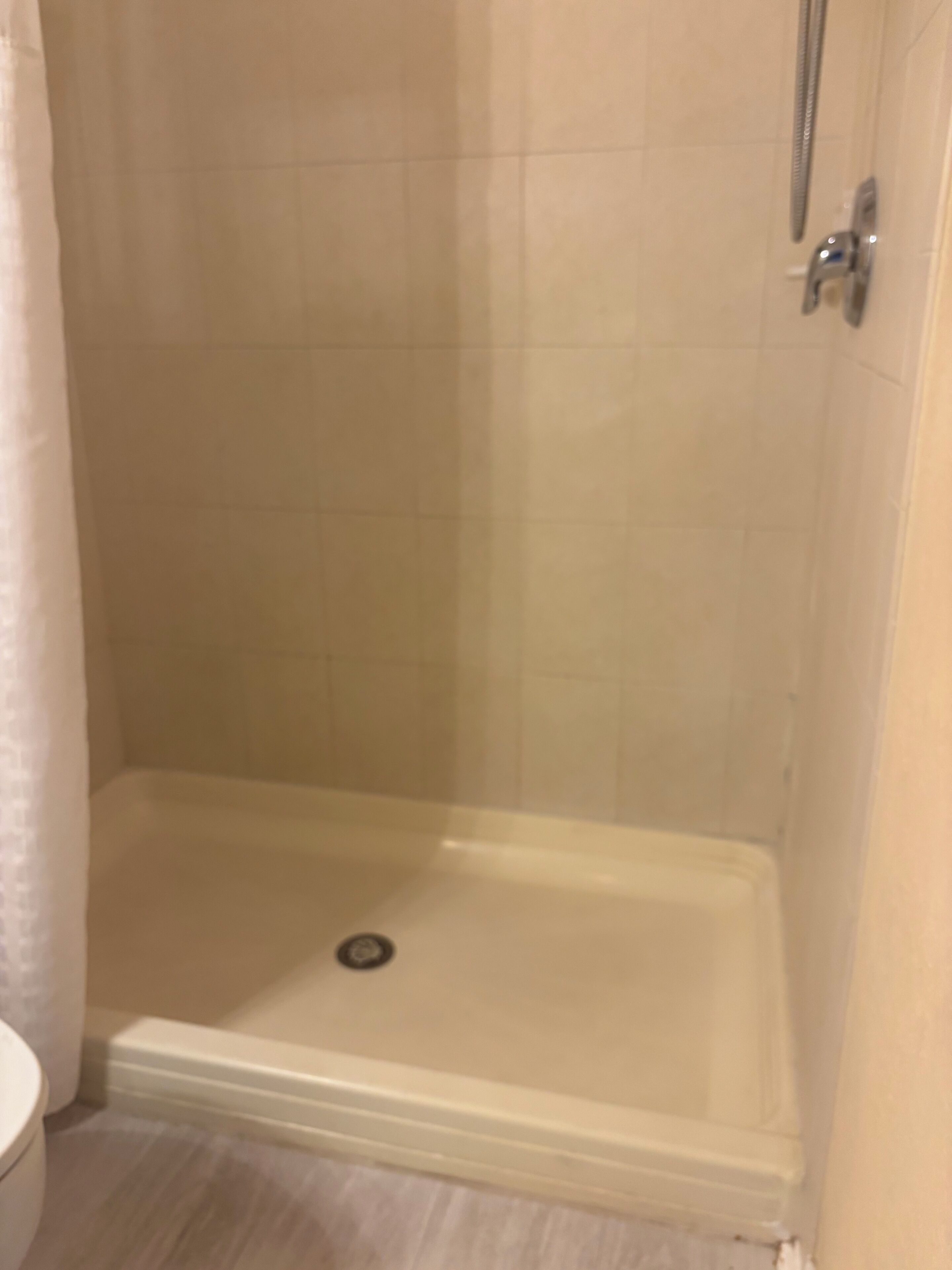 A shower with a drain, a toilet, and a tiled wall.