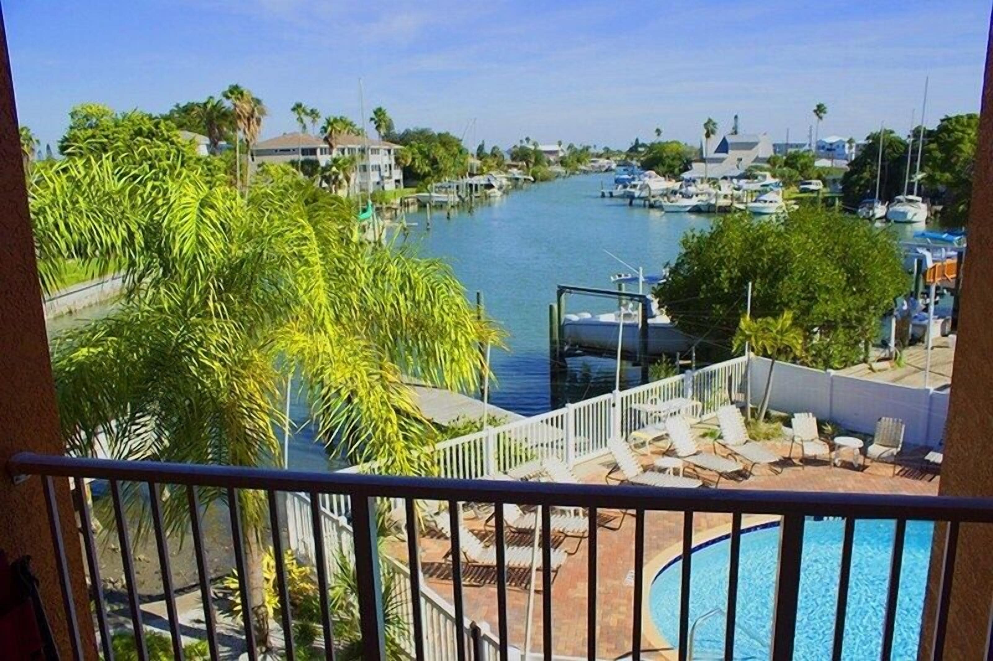 A view from a balcony overlooking a marina with boats, a swimming pool, and palm trees.