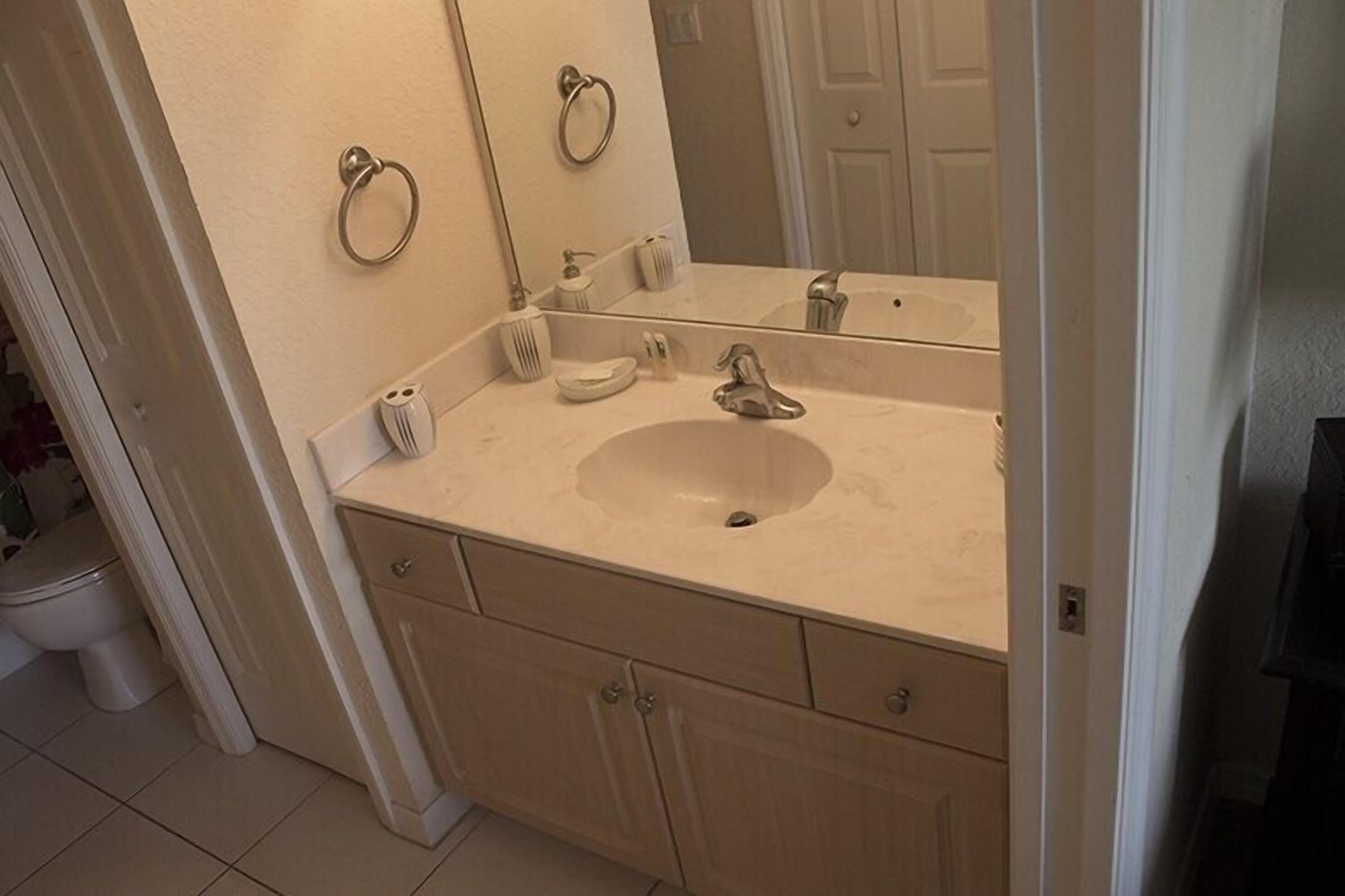 Un baño con lavamanos, espejo, toalleros y retrete.