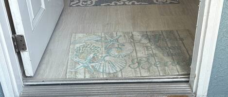 A doorway with a patterned rug, a doormat with sea-themed designs, and a wooden floor.