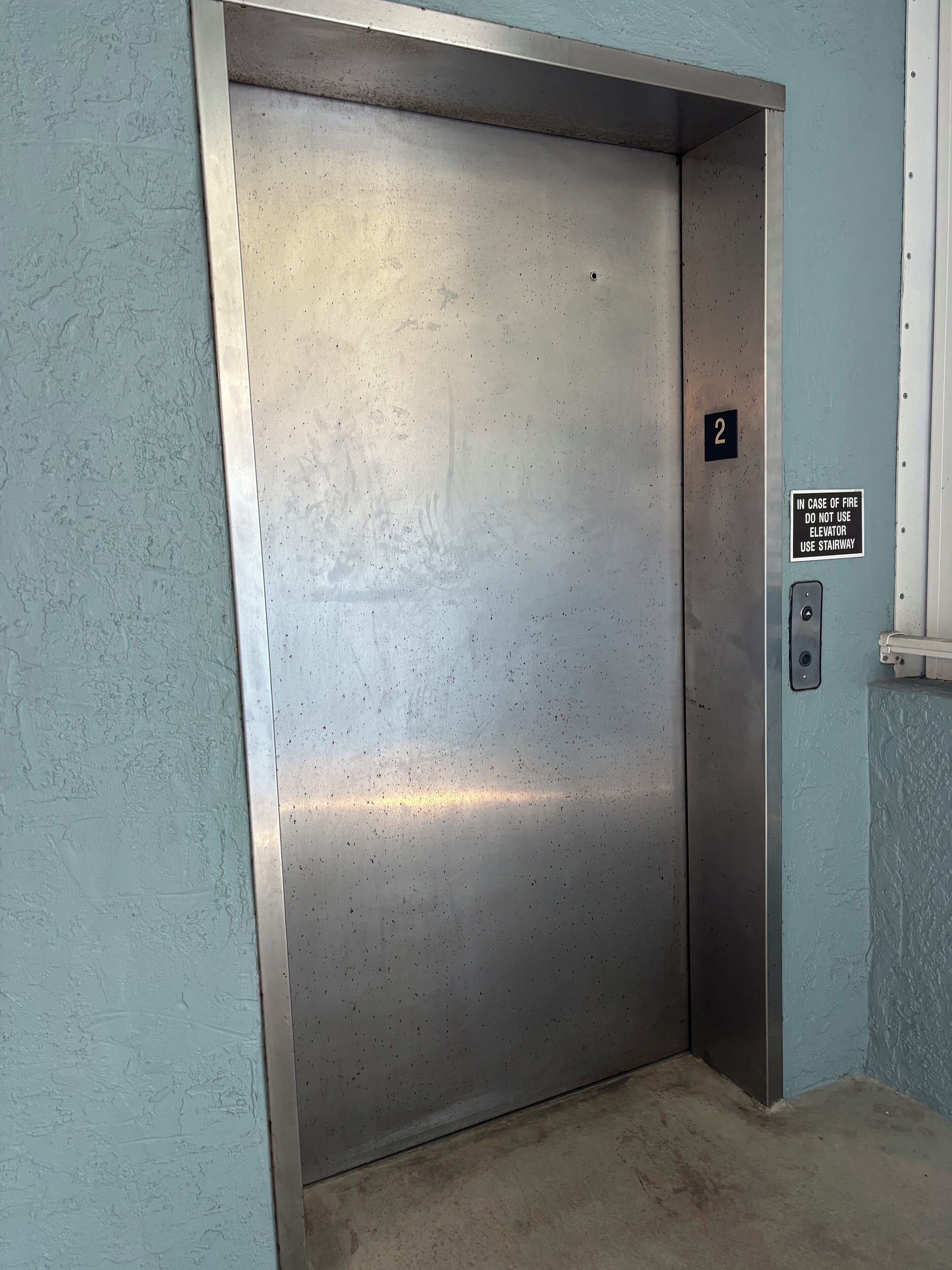 Puerta metálica de ascensor con el número 2 y un cartel de seguridad.