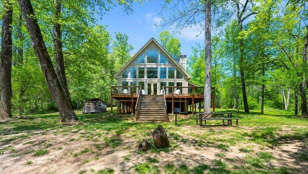 Eine Lodge mit Glasfassade, einer Holterrasse und einem Picknicktisch in einer Waldlandschaft.