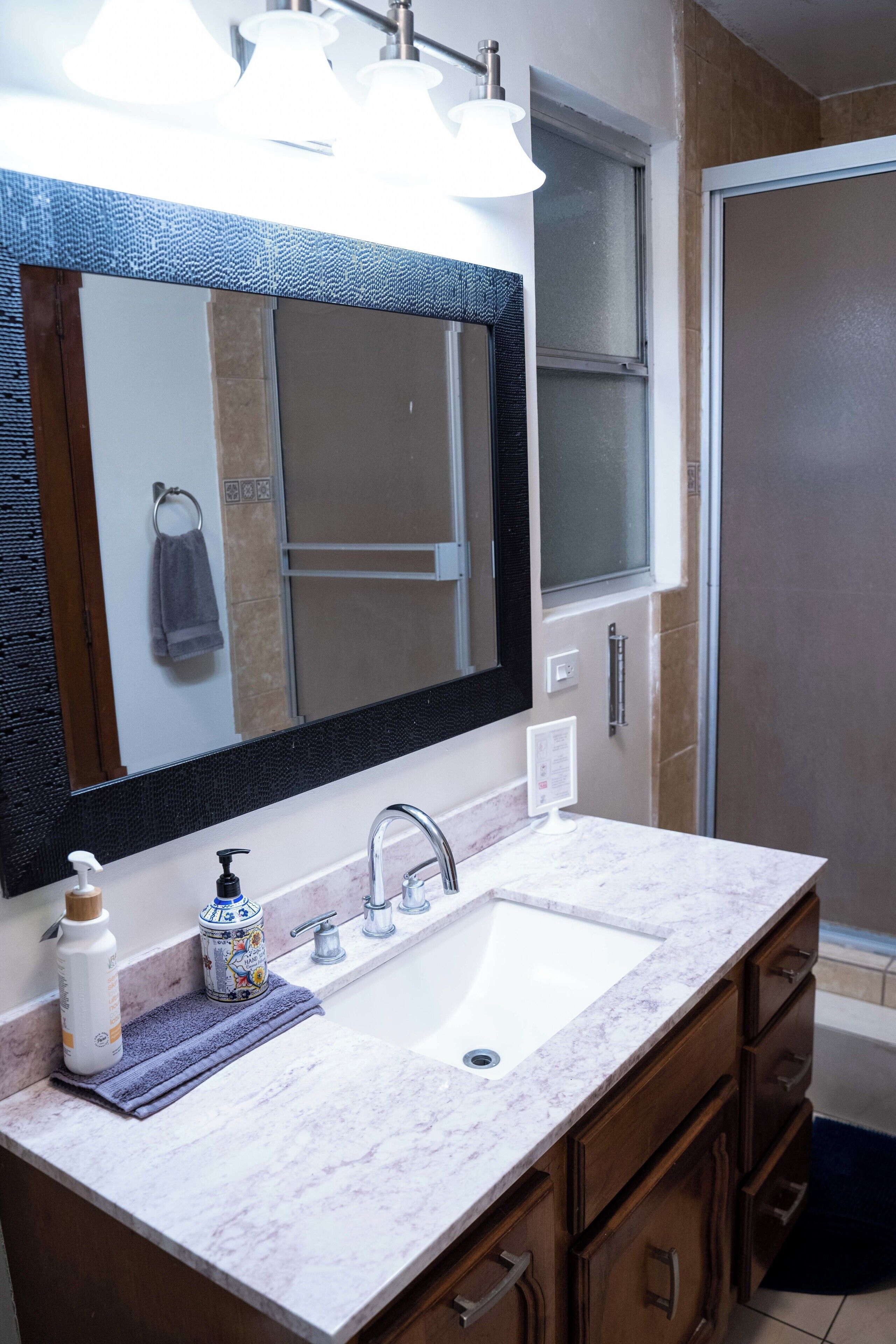 A bathroom with a large mirror, a sink, a towel rack, and a shower door.