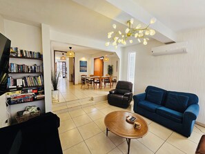A living room with a blue sofa, a coffee table, a bookshelf, and a dining area with a table and chairs.