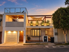 A two-story residential building with a garage, a balcony, and potted plants.