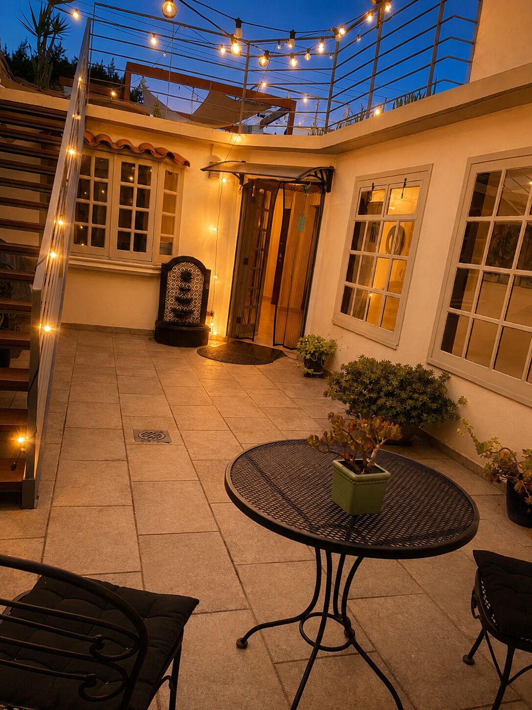 A patio with a round table, chairs, potted plants, and string lights.