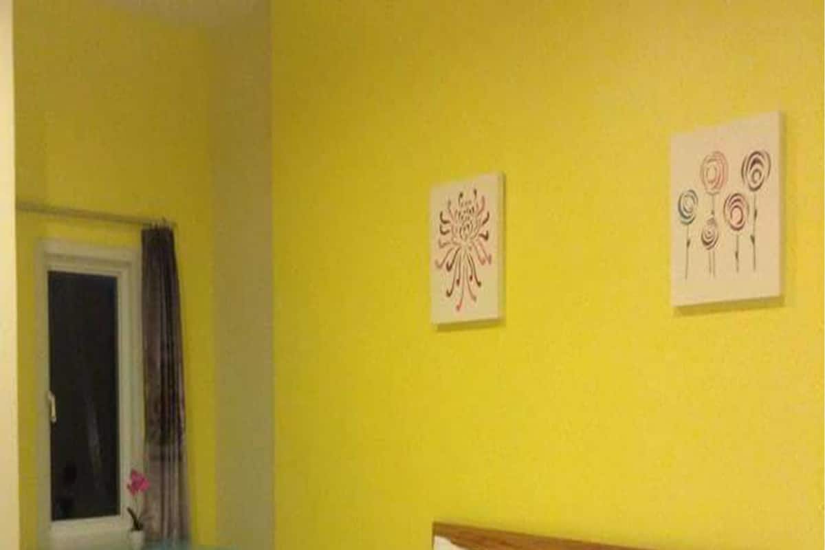 A bed in a room with yellow walls, a wooden headboard, and two artworks on the wall.