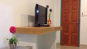 A compact room with a small refrigerator, a television on a wooden shelf, and a door with a teal frame. - The Moonlight Resort (Ban Chang)