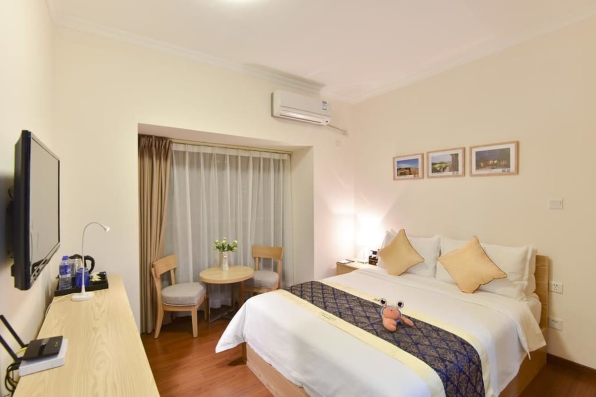 A hotel room with a bed, a desk, a chair, a TV, and an air conditioner.