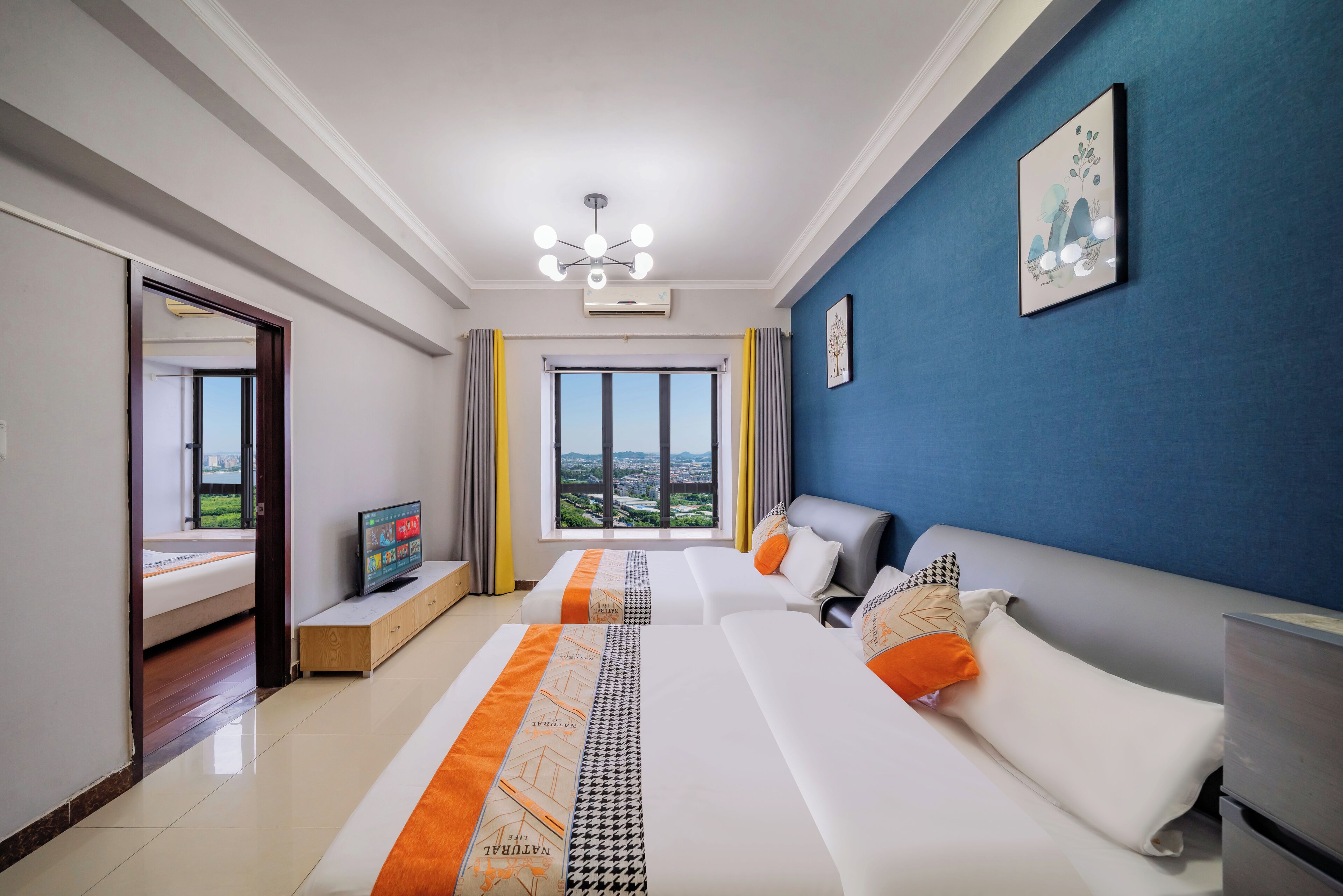 A modern hotel room with a large bed, a sofa, a TV, and a view of the city.