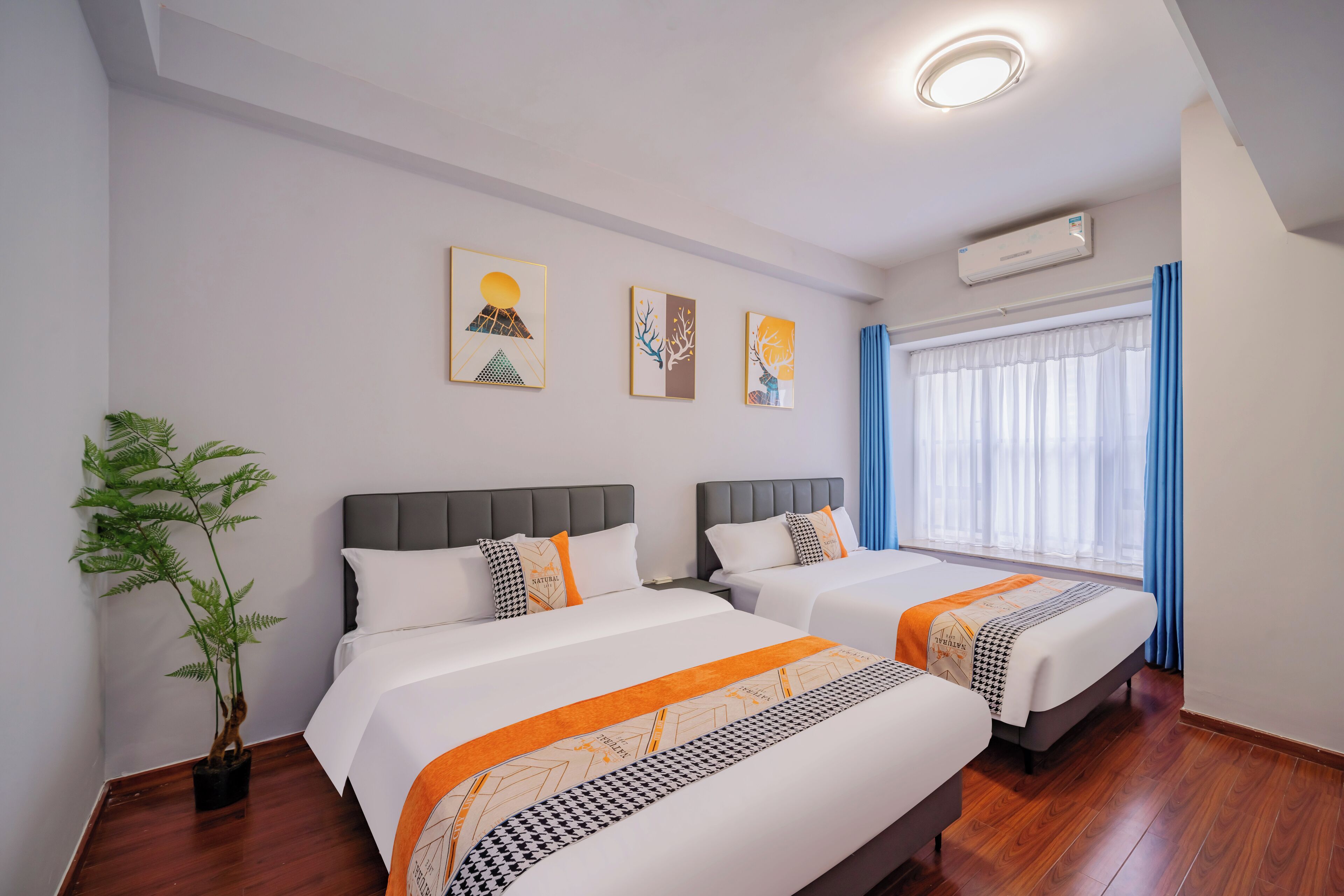 Une chambre d’hôtel avec deux lits, une plante en pot, des œuvres d’art accrochées au mur et un appareil de climatisation.
