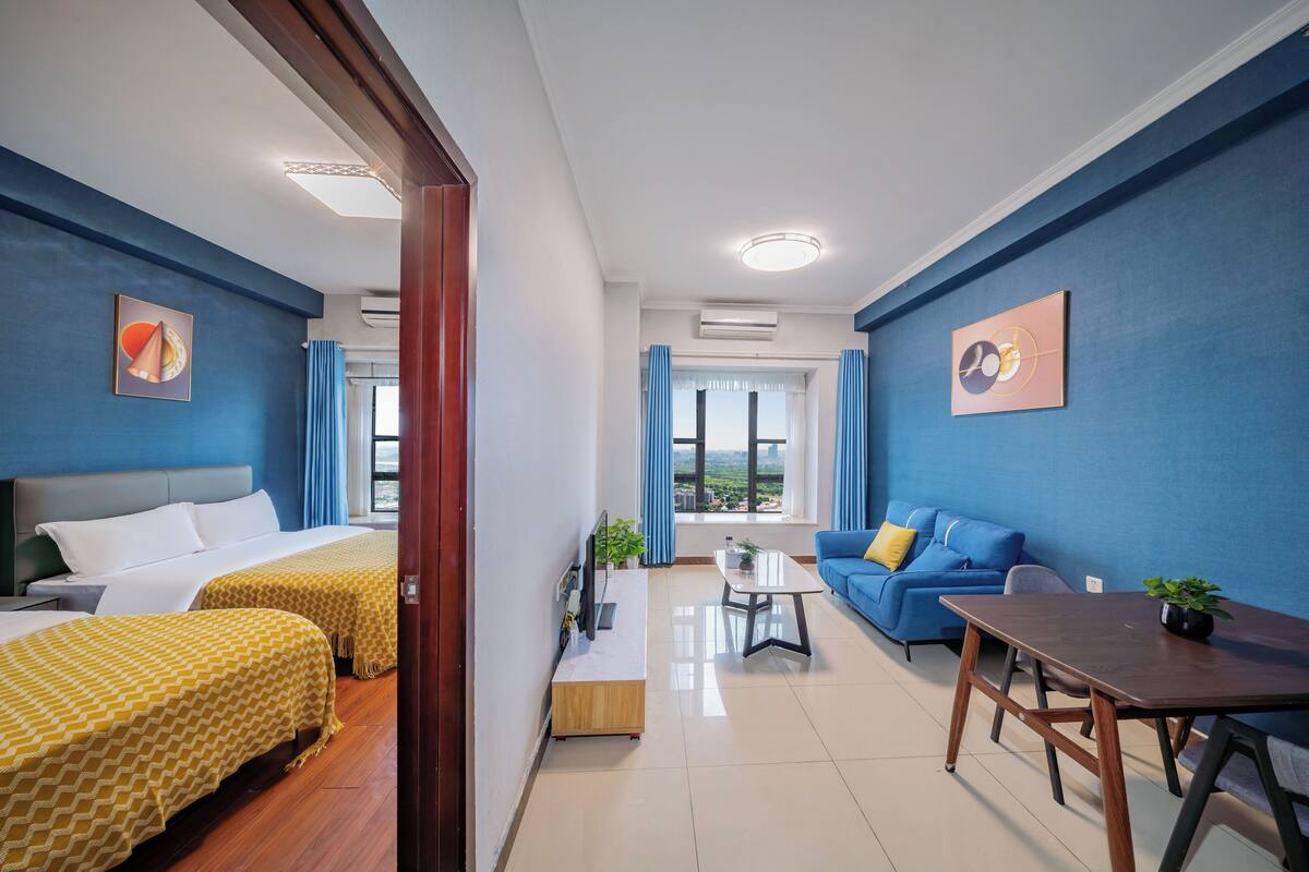 A hotel room with two beds, a sofa, a dining table, and a view of the outdoors.