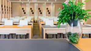 Un comedor moderno con mesas y sillas, un jarrón decorativo con plantas verdes y un diseño geométrico en la pared.