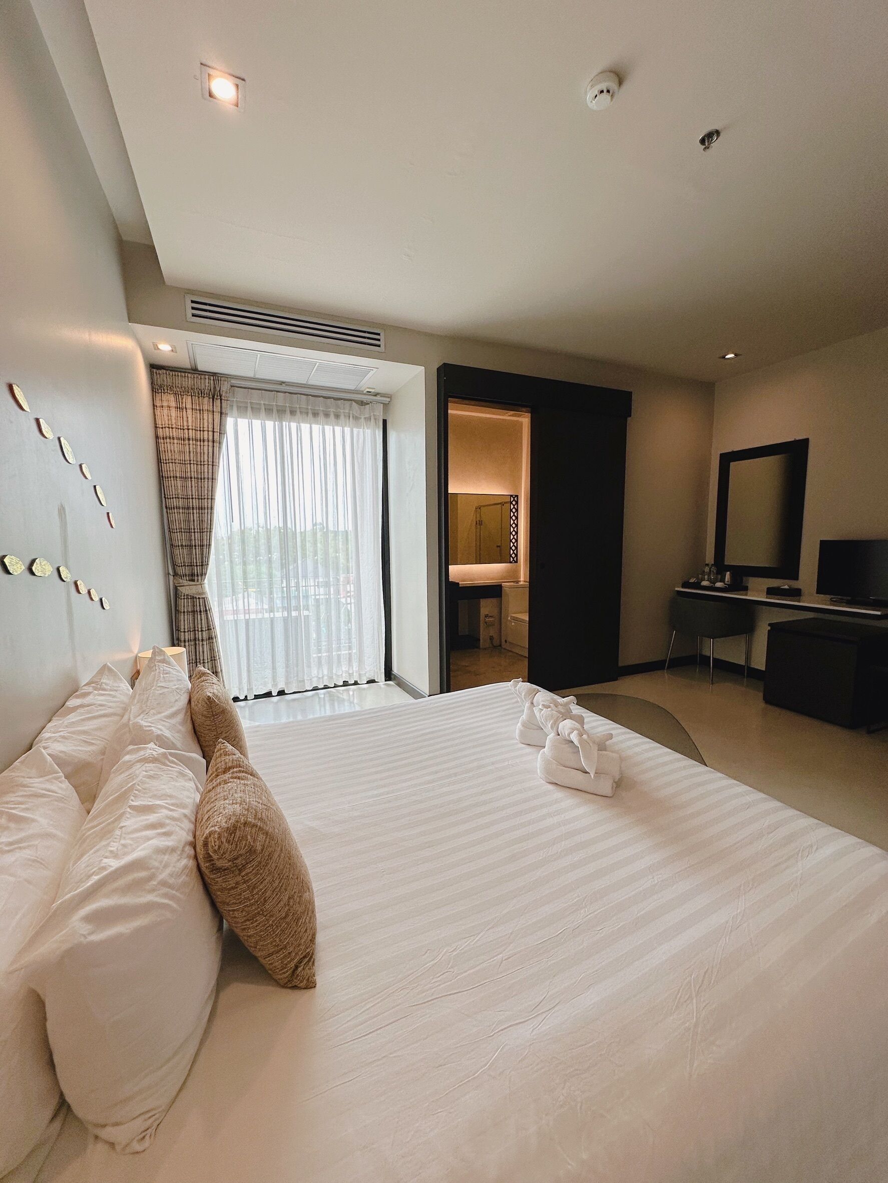 A hotel room with a large bed, a desk, a TV, and a bathroom visible through an open door.
