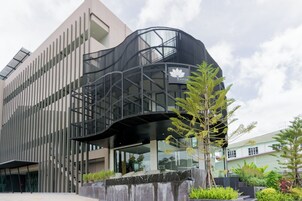 Un edificio moderno con fachada de vidrio curva, una estructura metálica negra destacada y un logotipo con una hoja de arce.
