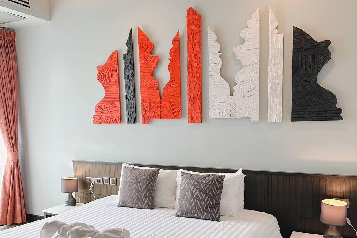 A hotel room with a large bed, a headboard, a bedside table with a lamp, and a wall with abstract art pieces.