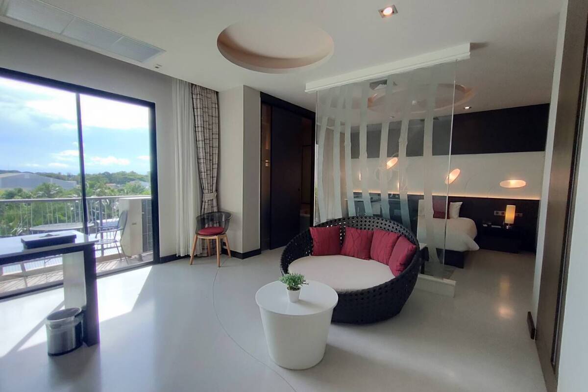 A modern living room with a large window, a round black and red sofa, a white coffee table, and a glass partition.