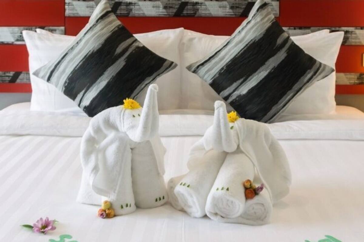 A hotel room with a bed, pillows, and a nightstand with a lamp.