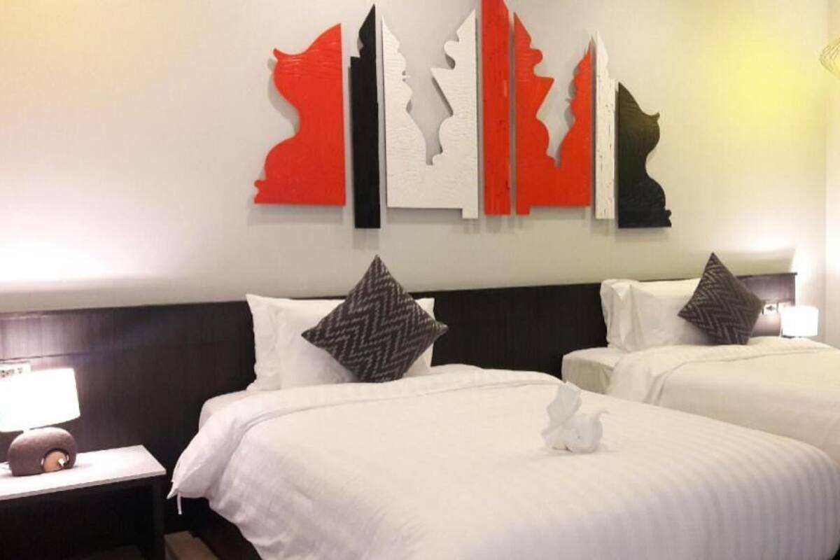 A hotel room with two beds, a nightstand with a lamp, and a wall with abstract art.