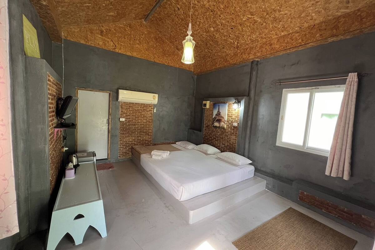 A bedroom with a bed, a desk, a mirror, and a window.
