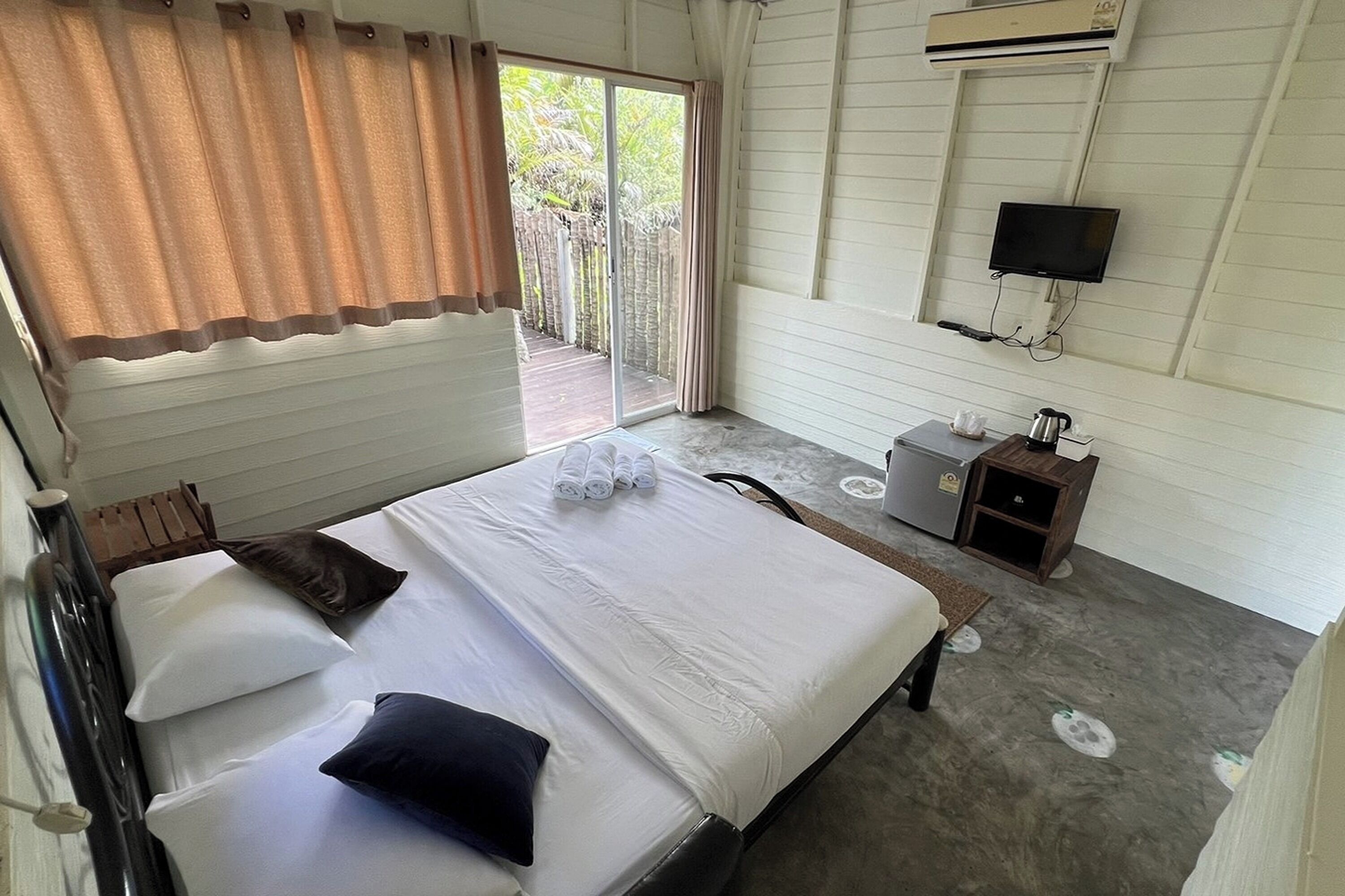 A hotel room with a bed, a TV mounted on the wall, and a small desk with a kettle.