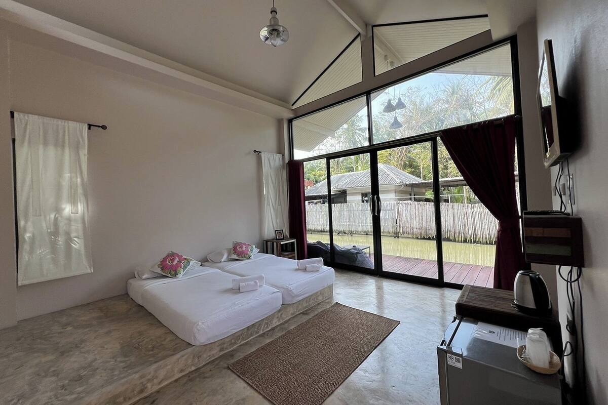 A modern room with a large sliding glass door leading to a deck, a sofa bed with pillows, a coffee maker, and a flat-screen TV mounted on the wall.