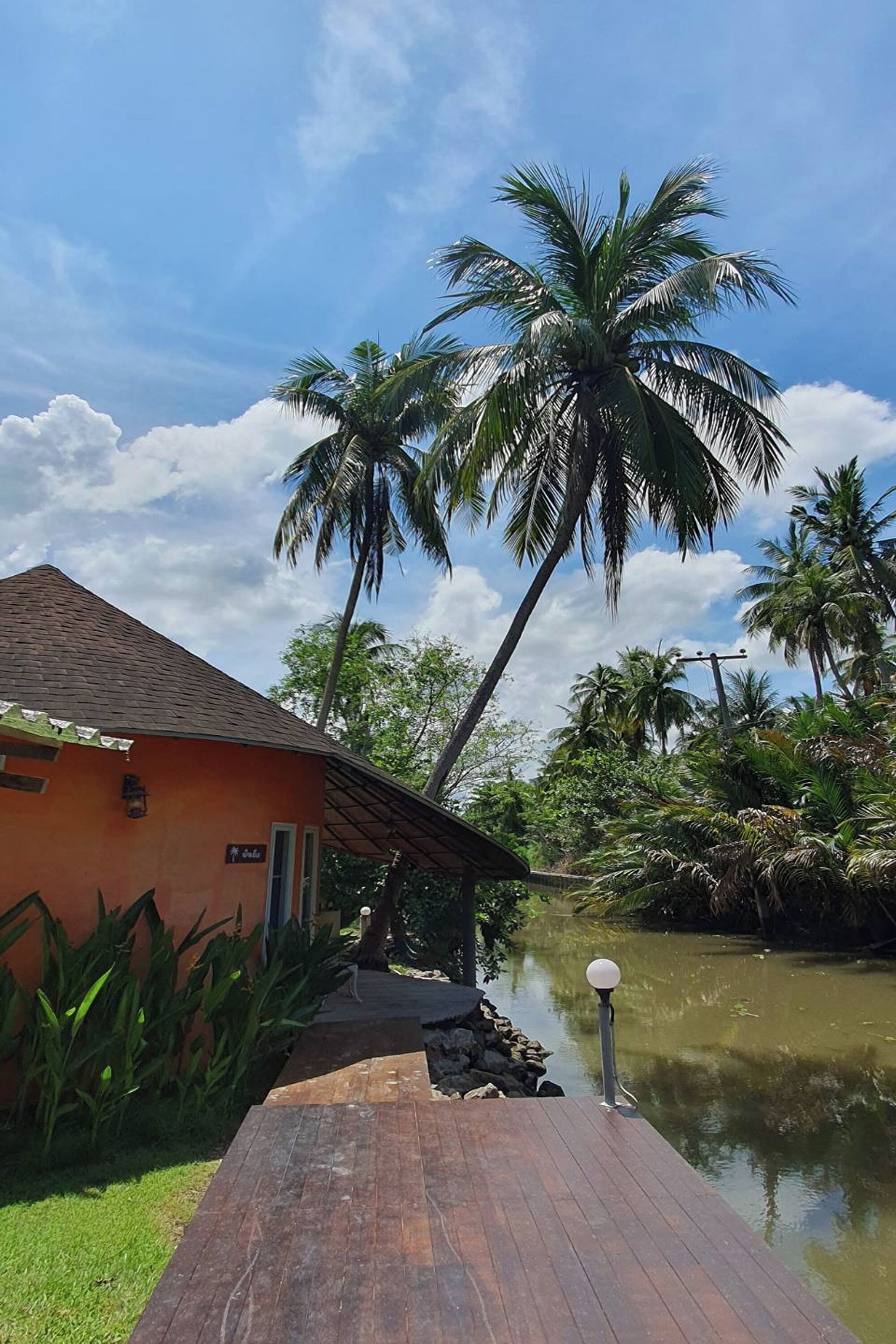 A wooden dock leading to a building with a tiled roof, surrounded by palm trees and a calm water body.