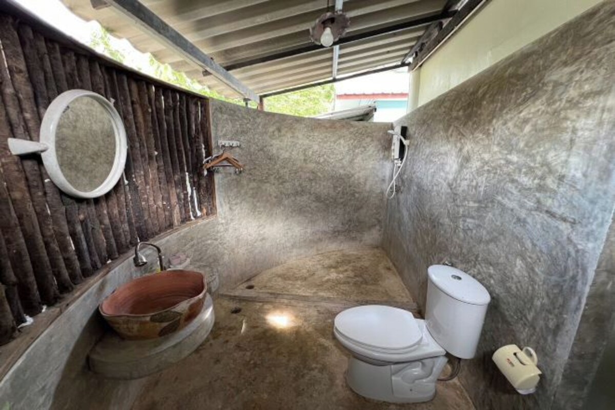 A small, rustic bathroom with a wooden door, a round mirror, a simple sink, and a toilet.