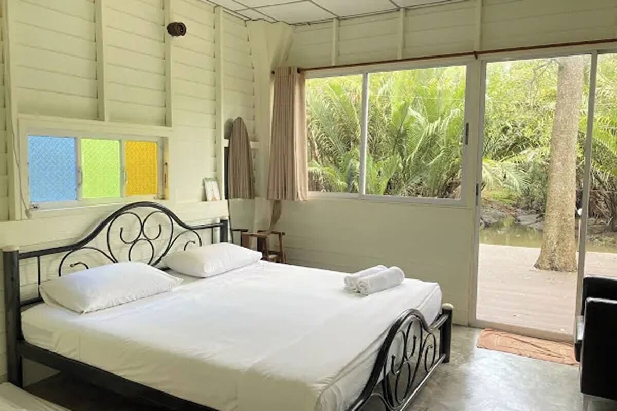 A bedroom with a bed, a window with curtains, and a view of greenery outside.