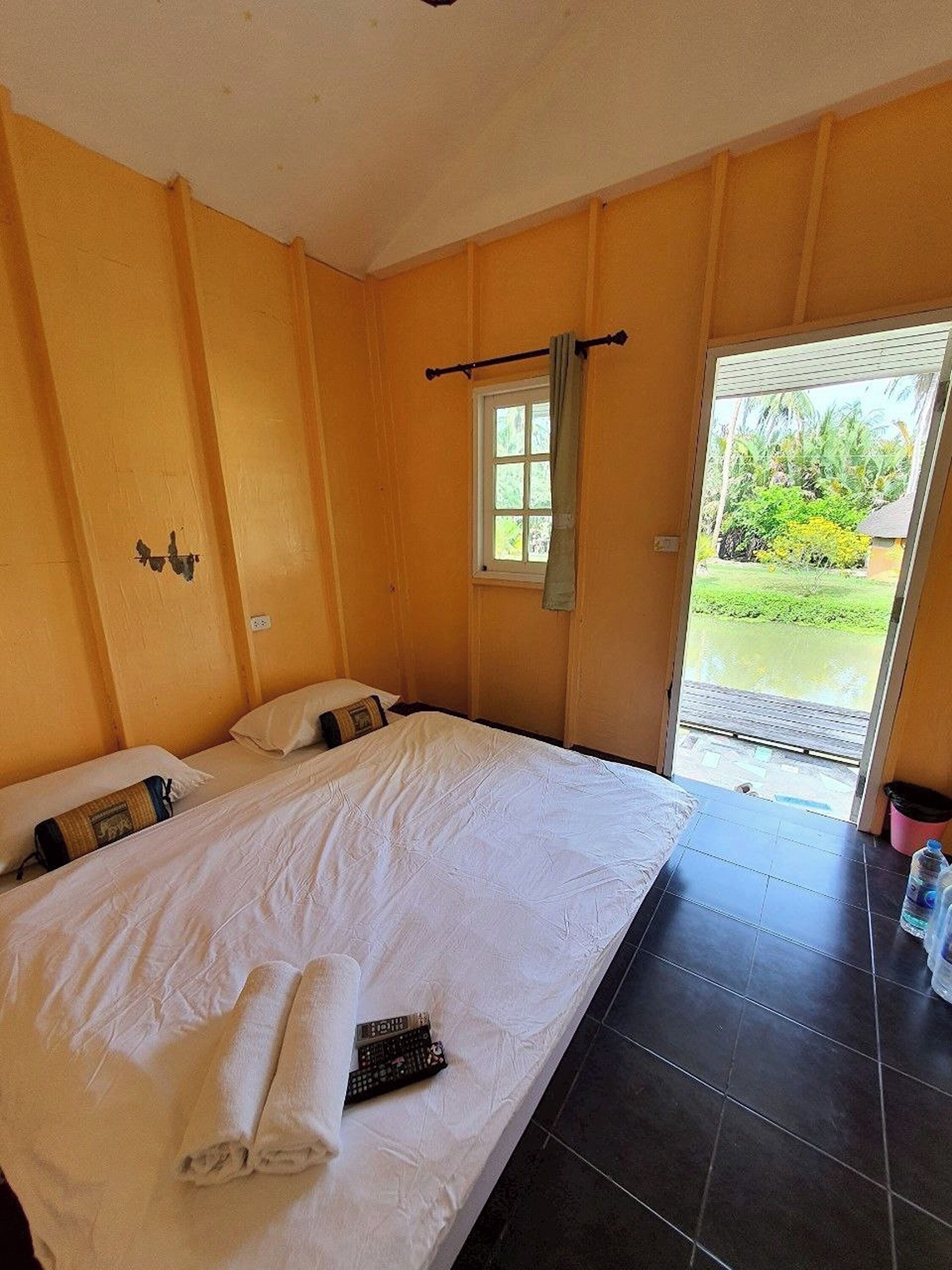 A hotel room with a bed, a window, and a view of greenery outside.