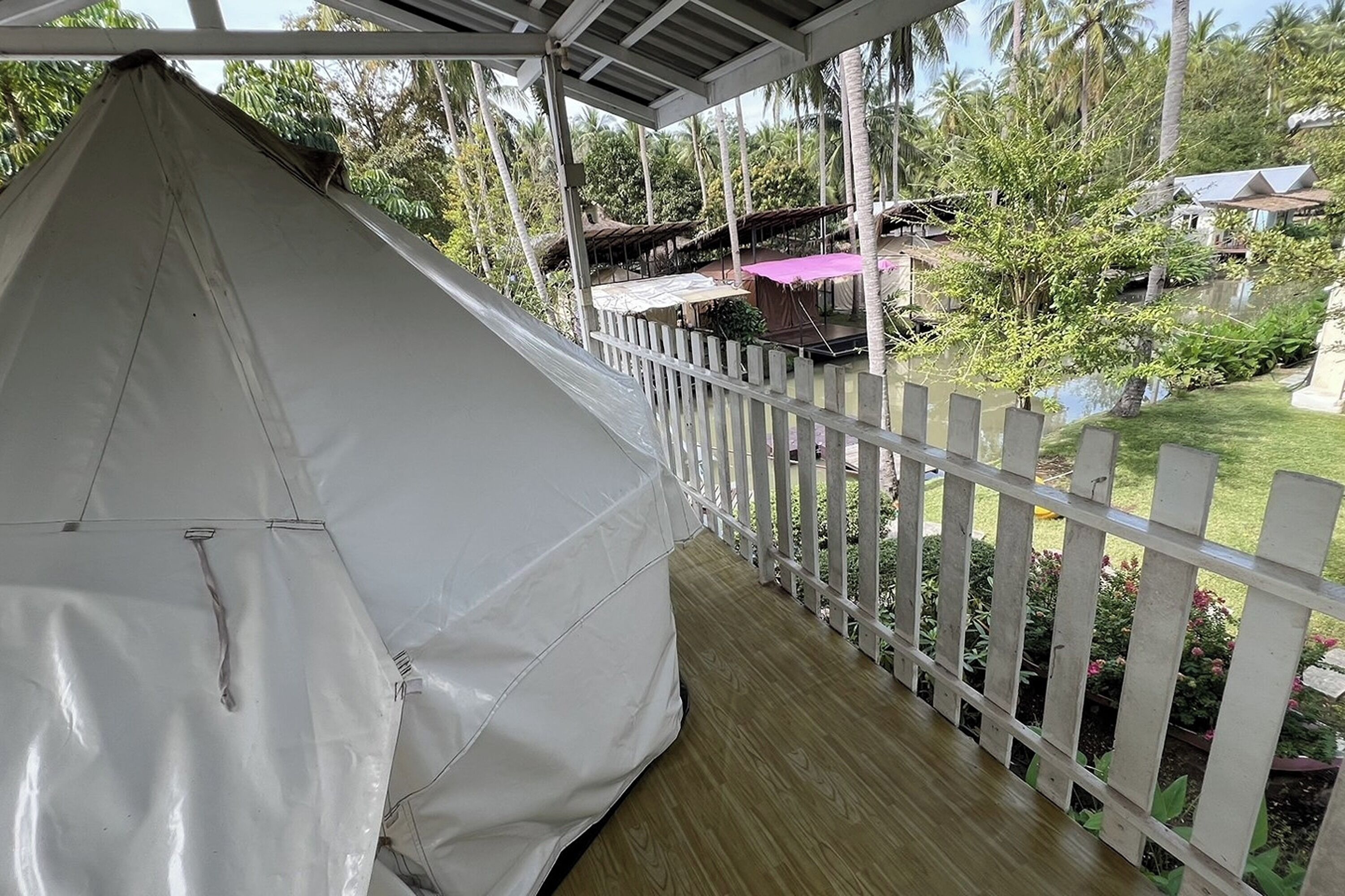 A covered outdoor area with a white tent, wooden deck, and white picket fence.