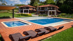 A swimming pool with lounge chairs, a covered patio, and a building with a tiled roof.