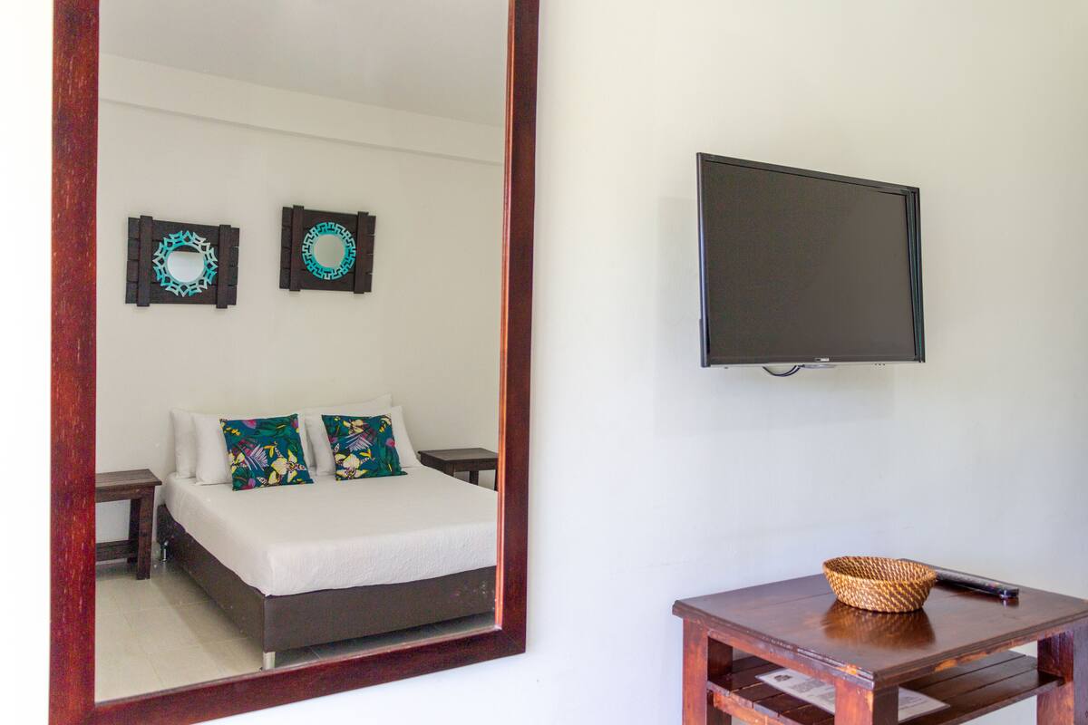 A bedroom with a bed, a mirror, a television, and a small table with a basket.