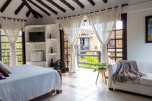 A bedroom with a bed, a TV, a fan, and a balcony with a view of greenery. - Finca Hotel Casa Nostra - Villa Mariana (Quimbaya)