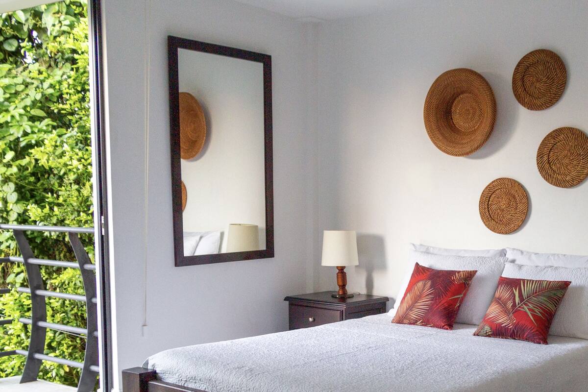 A bedroom with a bed, a nightstand, a lamp, a mirror, and wall decorations.