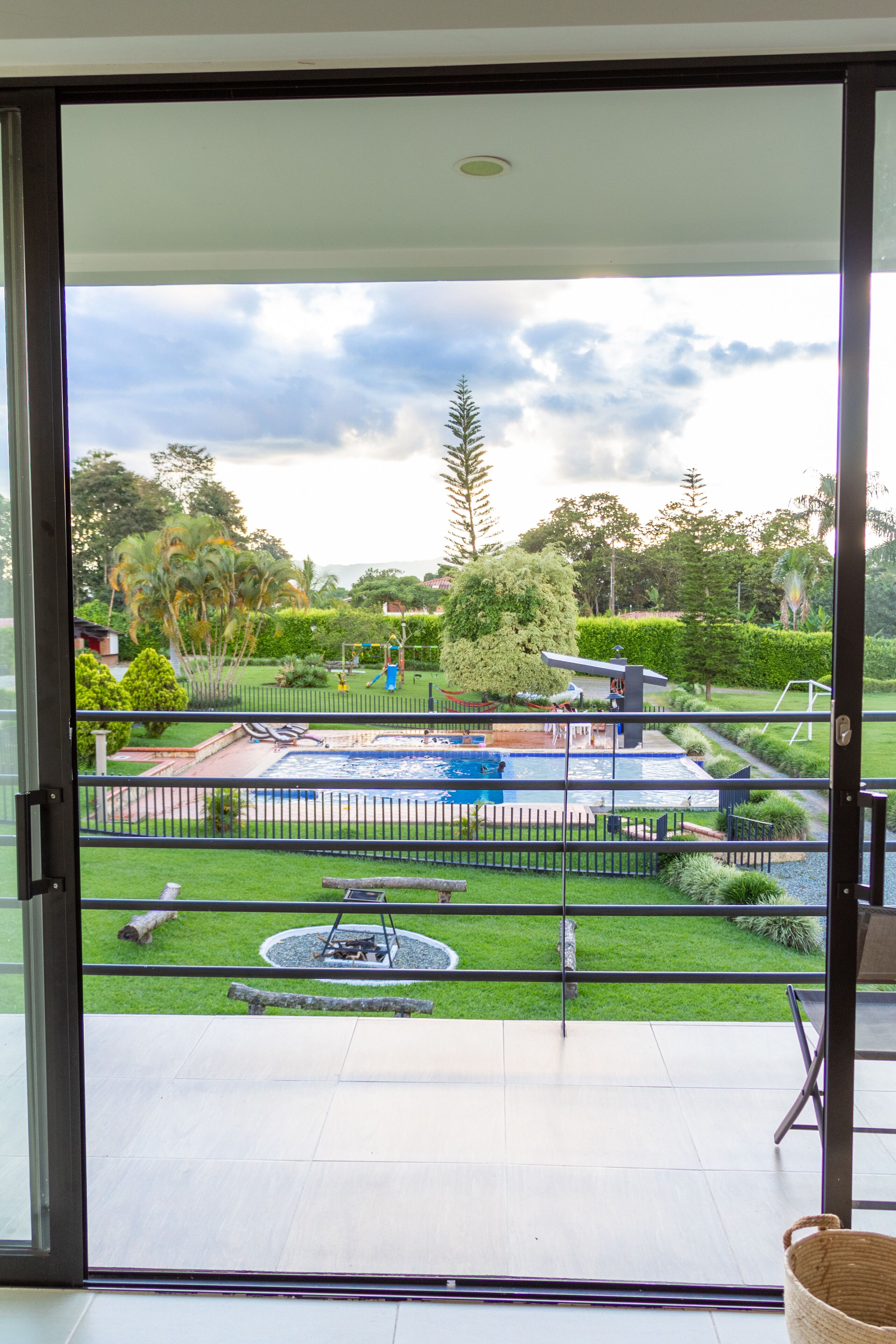 A view through a glass door of a backyard with a swimming pool, a fire pit, and a well-maintained lawn.
