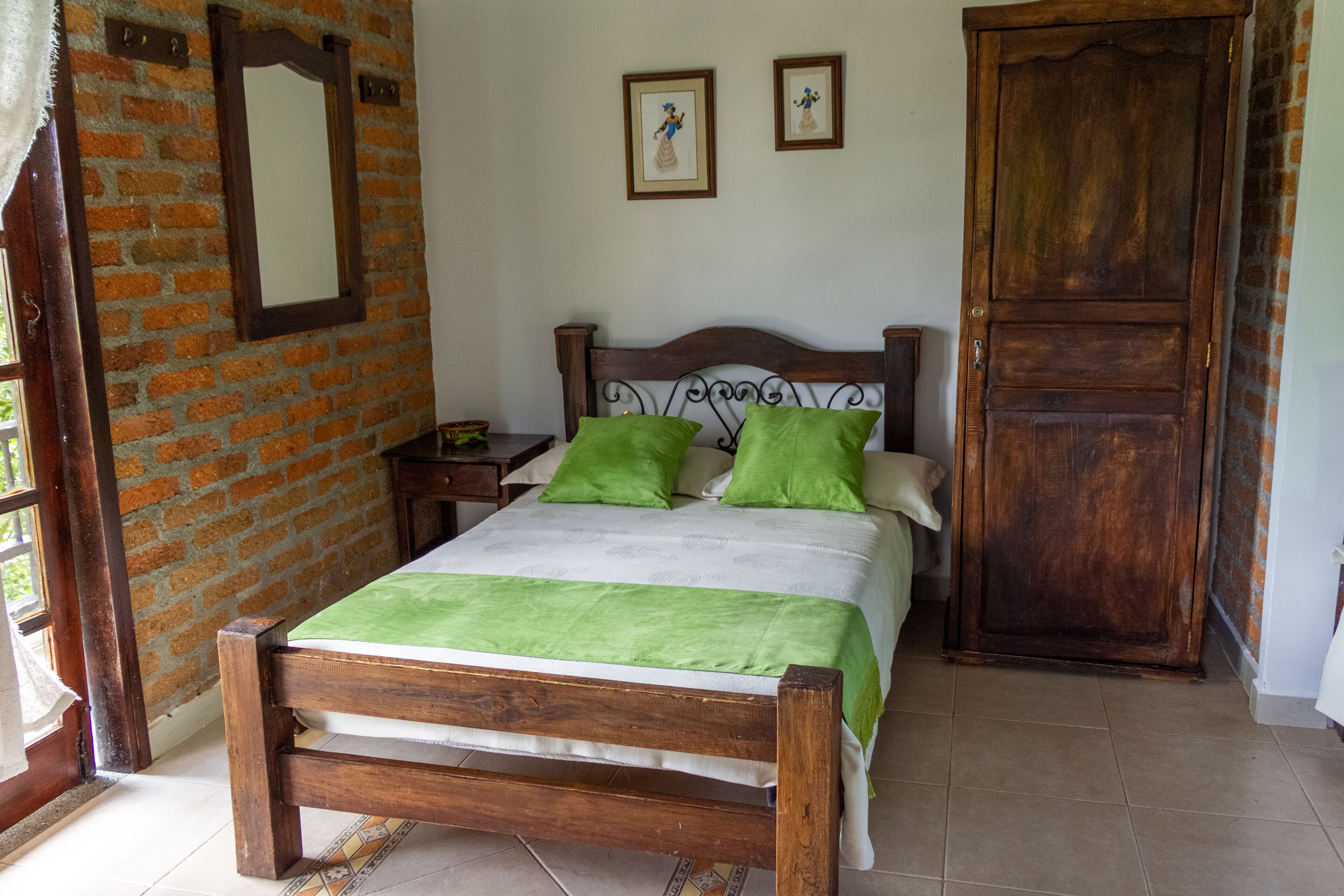 A wooden bed with green pillows, a brick wall, and a wooden door.