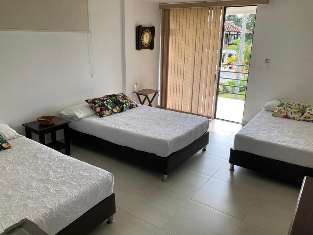 Habitación de hotel con dos camas individuales, una mesita pequeña, un reloj en la pared y una puerta corrediza al exterior.