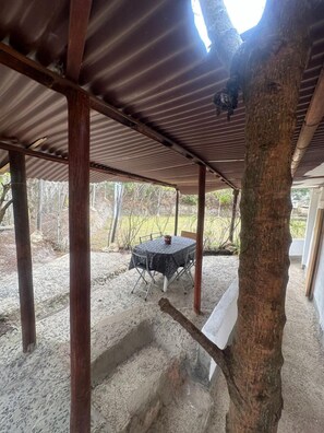 A covered outdoor area with a table and chairs, surrounded by trees and a sandy ground. - Hospedaje La Tierrita (Villa de Leyva)
