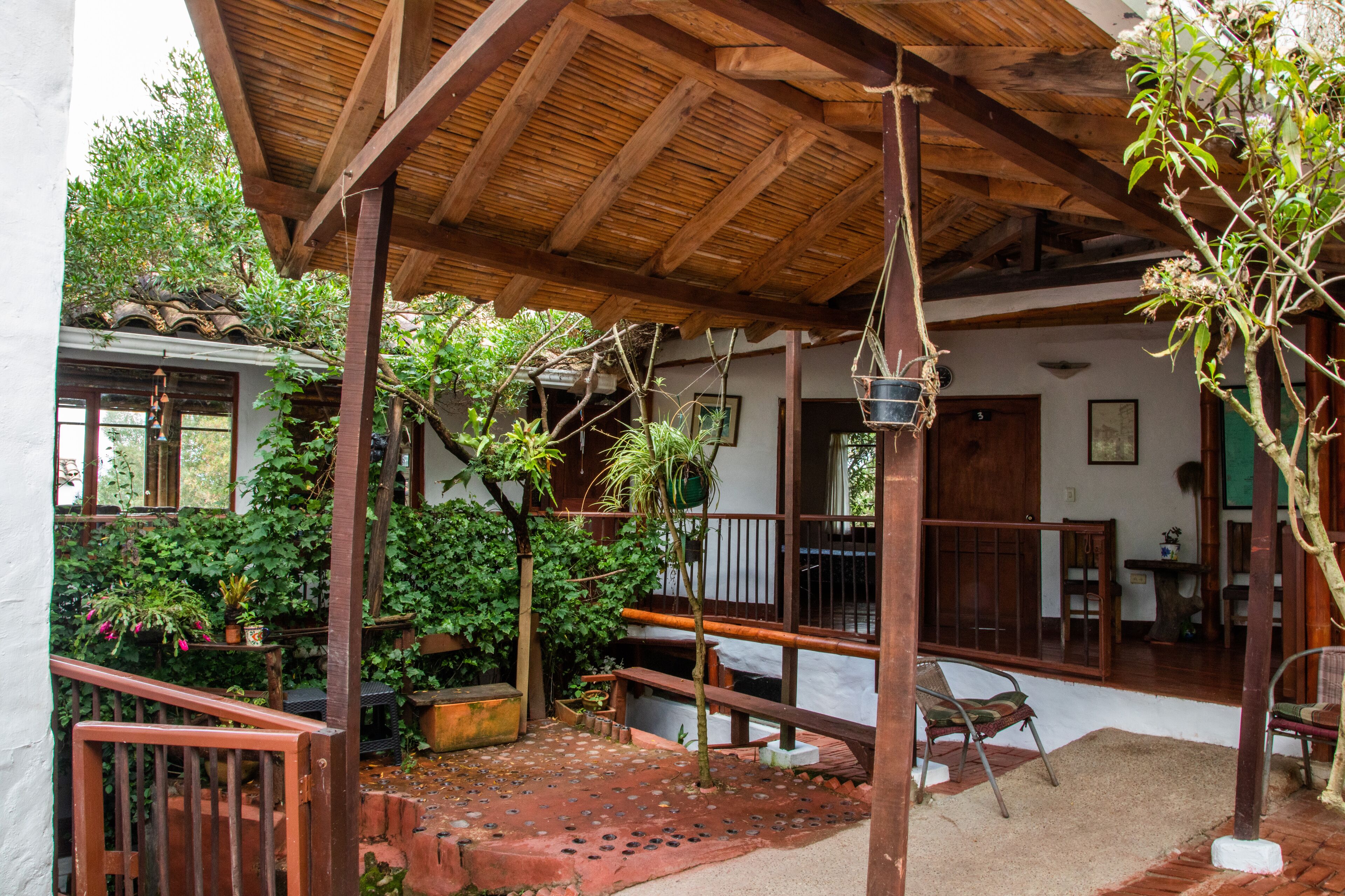 Un patio cubierto con techo de madera, plantas en macetas y un área de estar con sillas.