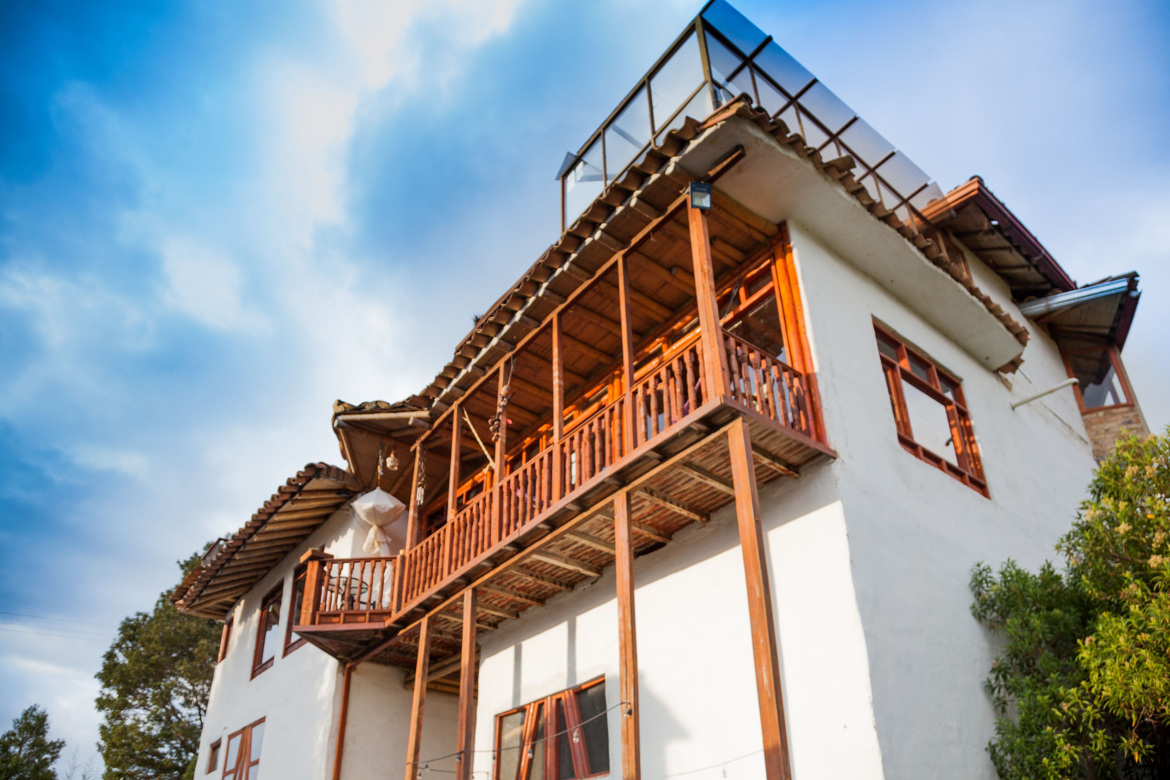 Un edificio de dos pisos con balcón, barandillas de madera y fachada blanca.