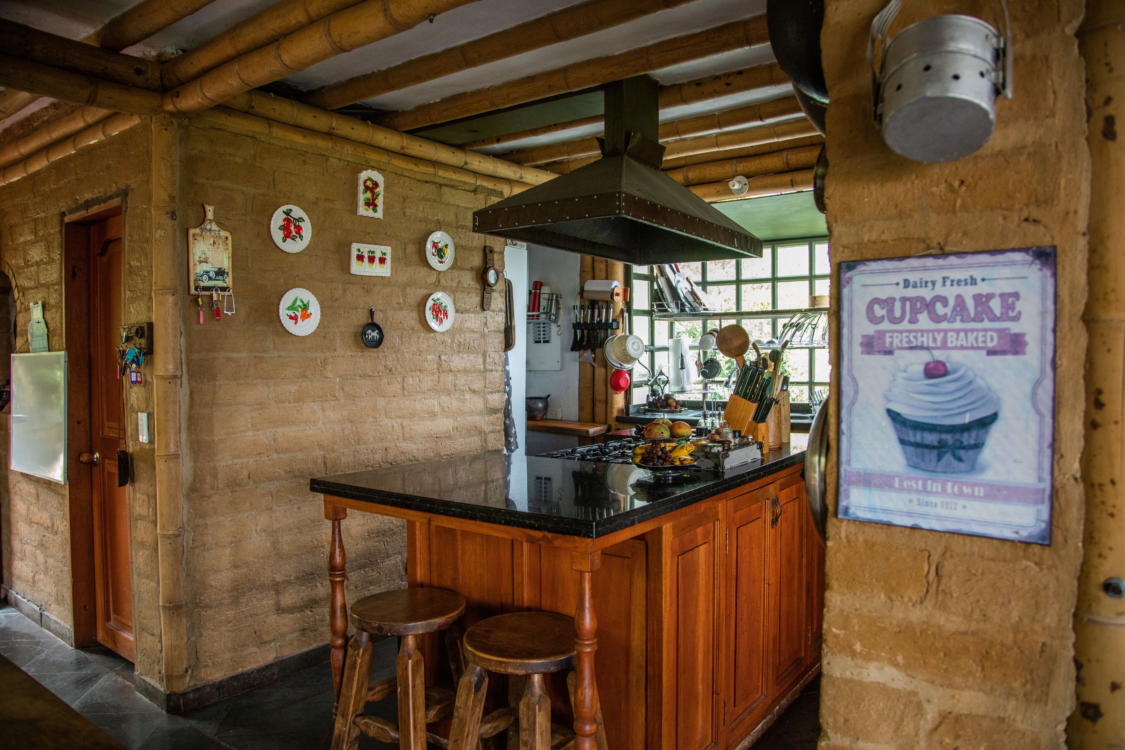 A rustic kitchen with a wooden bar, stools, and a large window.
