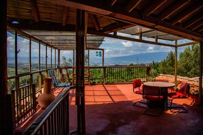 A covered outdoor area with a glass enclosure, red chairs, a table, and a large vase. - Hospedaje La Tierrita (Villa de Leyva)