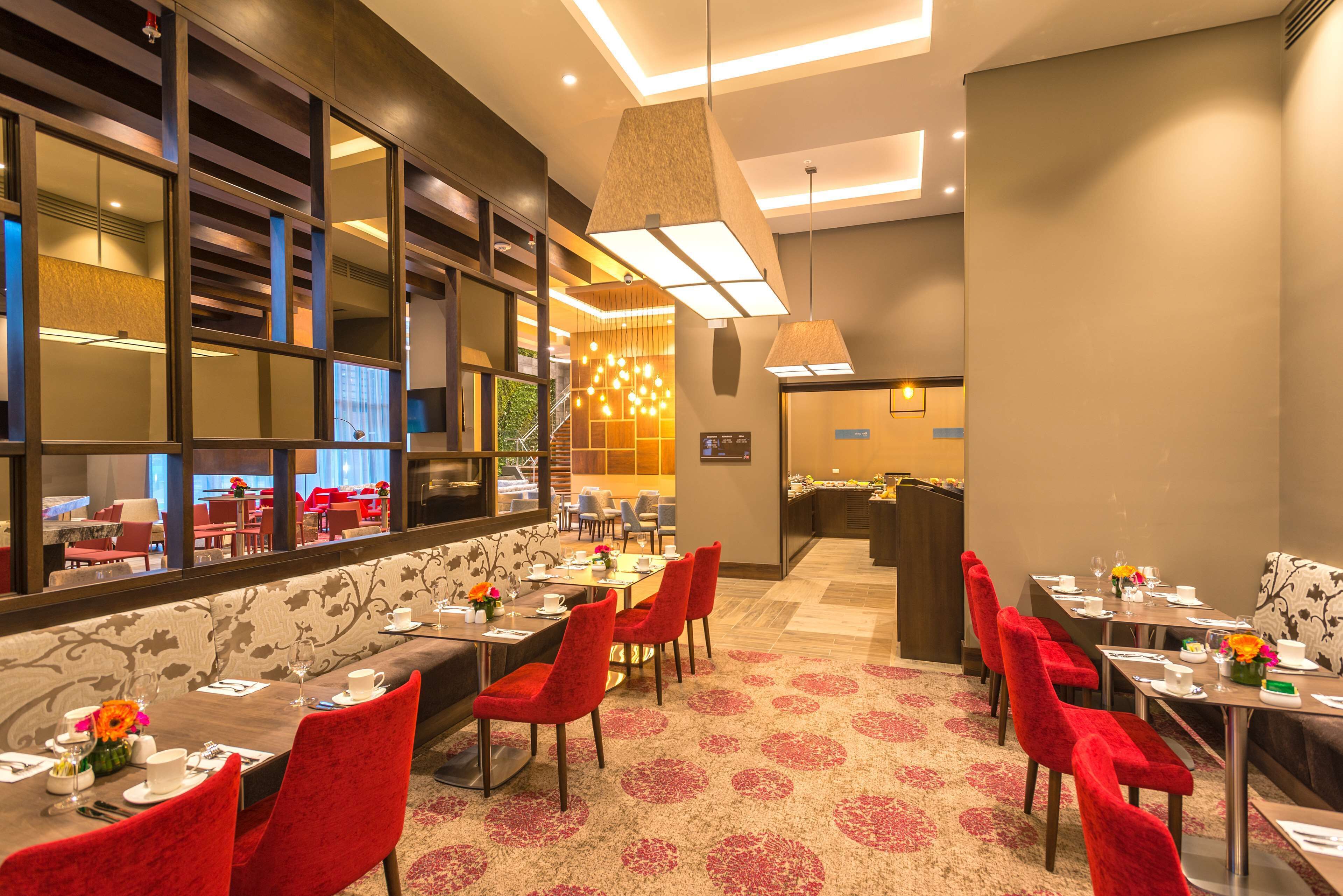 Une salle à manger d’hôtel avec plusieurs tables, des chaises à revêtement rouge et un tapis à motifs.