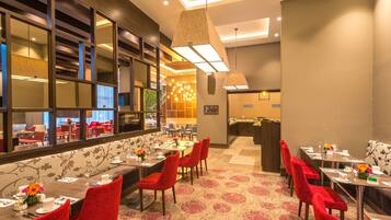 Une salle à manger d’hôtel avec plusieurs tables, des chaises à revêtement rouge et un tapis à motifs.